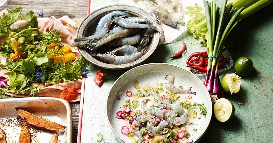 Garnelen Ceviche angerichtet auf einem weißen Teller. Neben Teller liegt eine Schale mit frischen unverarbeiteten Garnelen