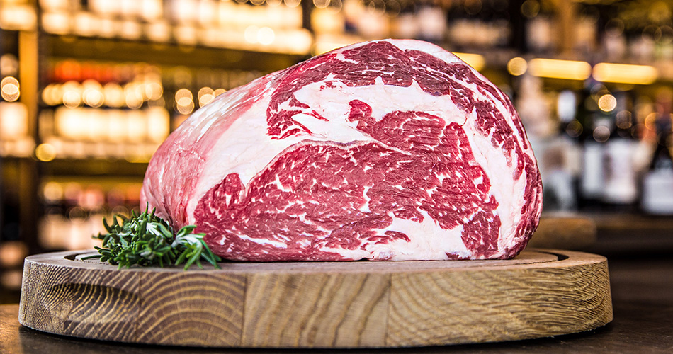 Sehr schoen marmoriertes Stueck Rindfleisch aus einem Holztablet angerichtet mit Thymian an der Seite